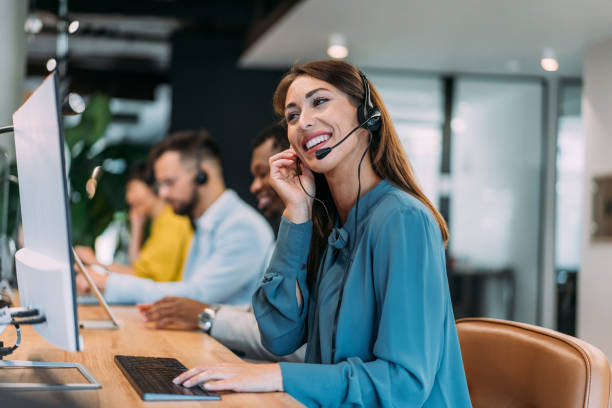 A support agent wearing a headset smiling at her desk, with colleagues working alongside her